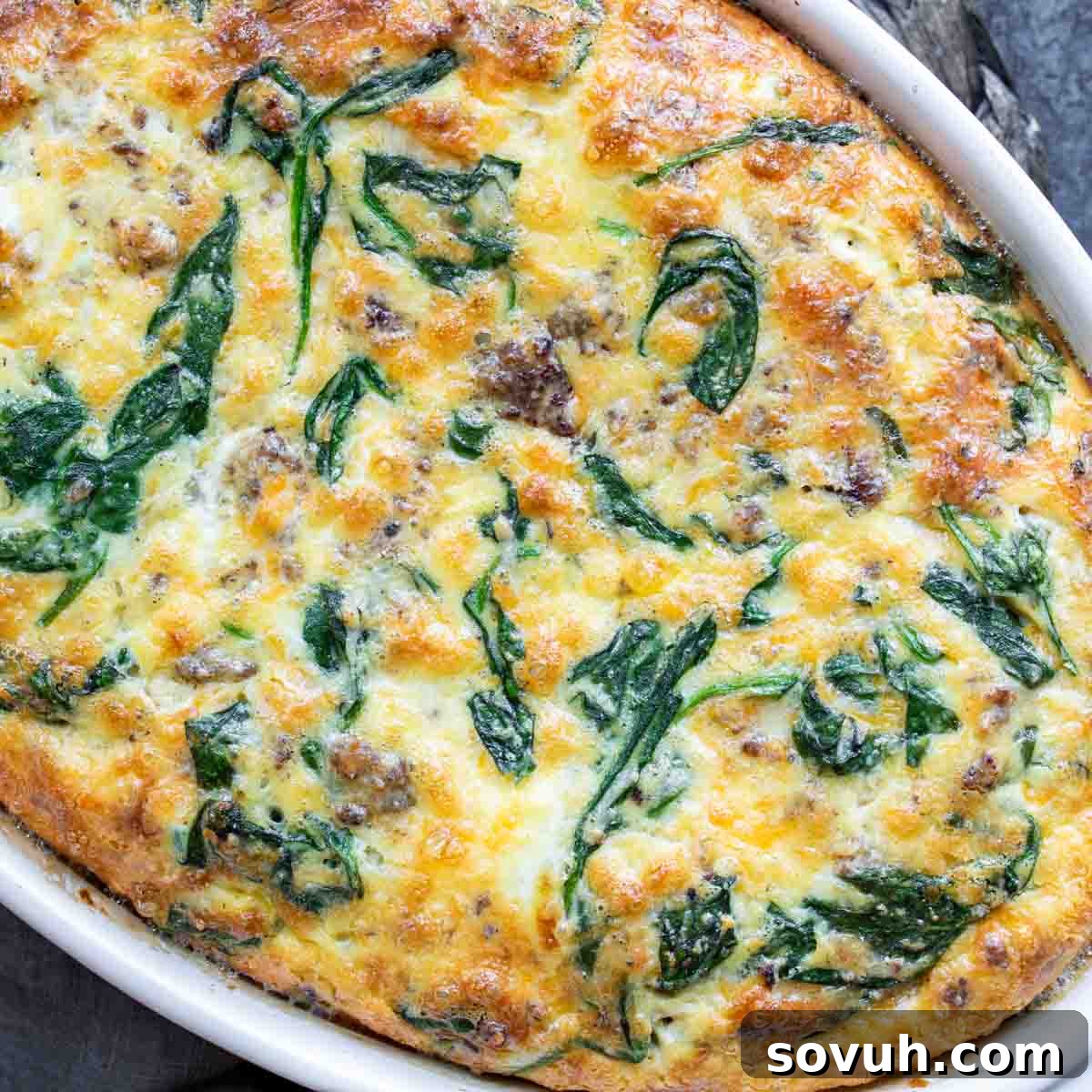 A freshly baked Sausage and Spinach Crustless Quiche, still in its white baking dish, showing a golden-brown top and slightly puffed texture.