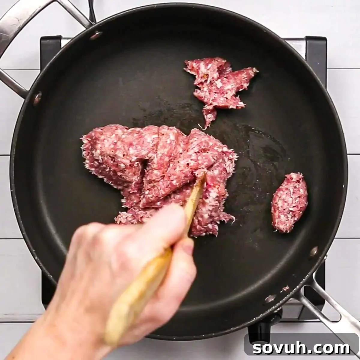 Ground breakfast sausage being broken apart and browned in a non-stick skillet over medium-high heat.