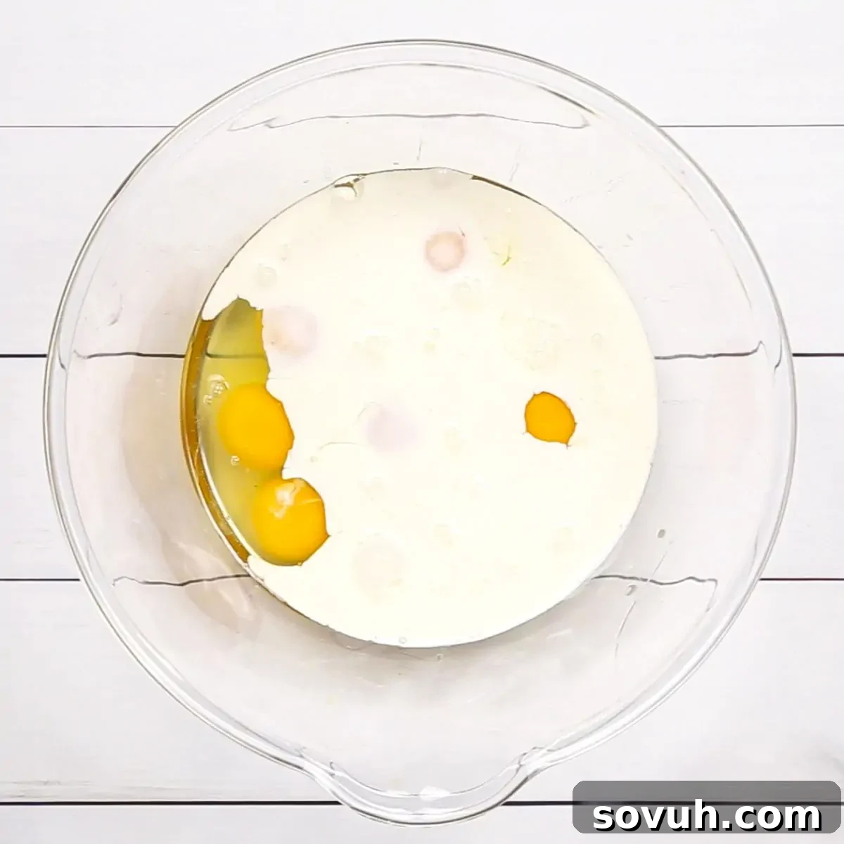 A mixing bowl containing cracked eggs and heavy cream, ready to be whisked for the quiche mixture.