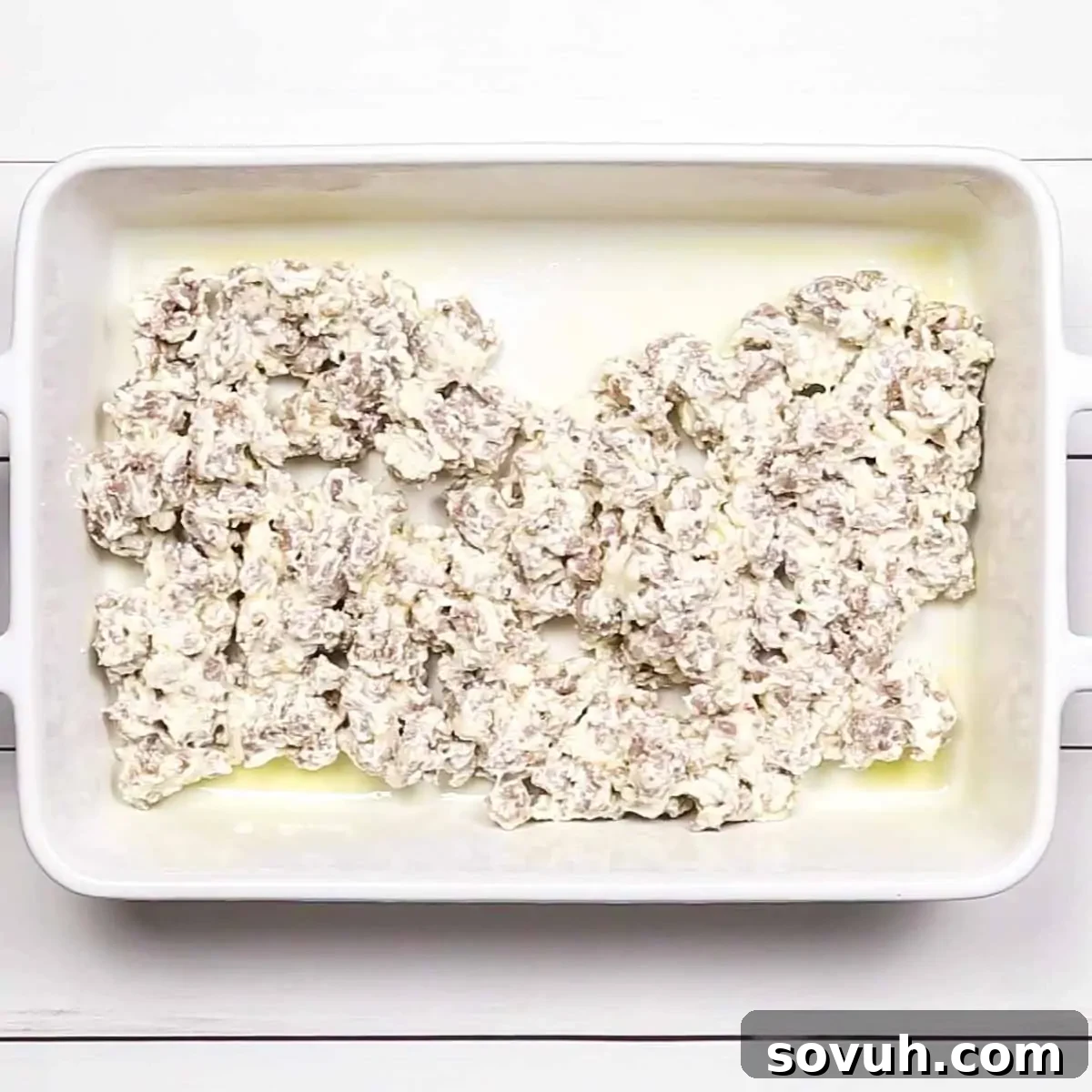 The sausage and cream cheese mixture spread evenly at the bottom of a greased white rectangular baking dish.