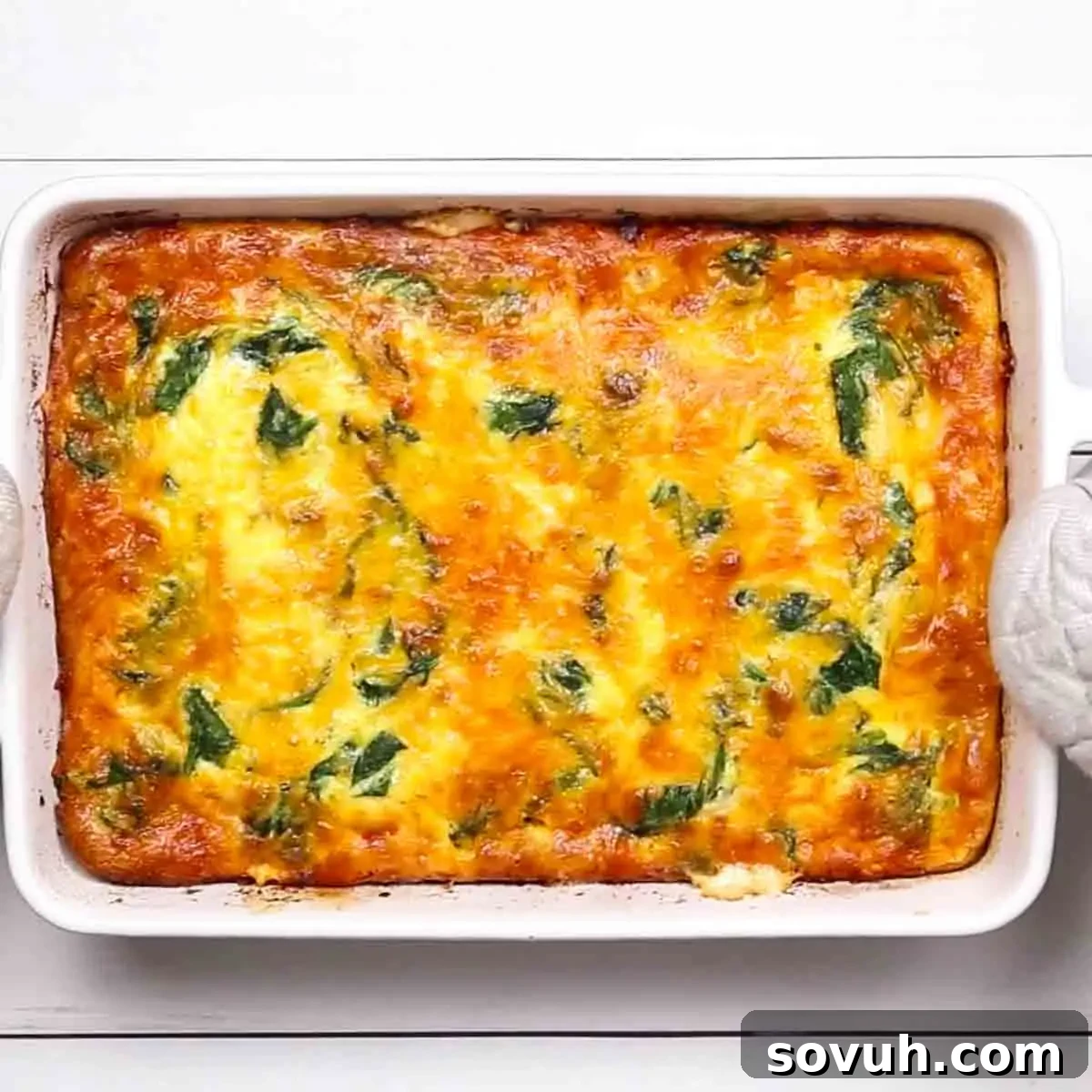 The baked Sausage and Spinach Crustless Quiche, golden-brown and slightly puffed, with melted cheese and visible spinach, cooling in the white baking dish.