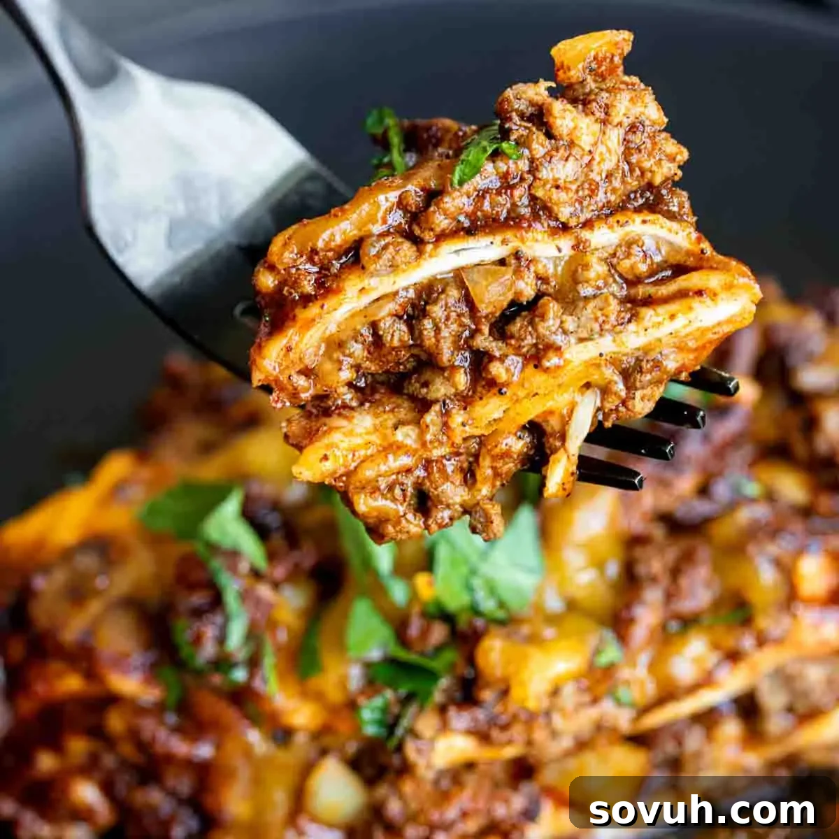 A fork is being used to pick up a piece of Beef Enchilada Casserole, showcasing layers of beef, cheese, and tortillas.