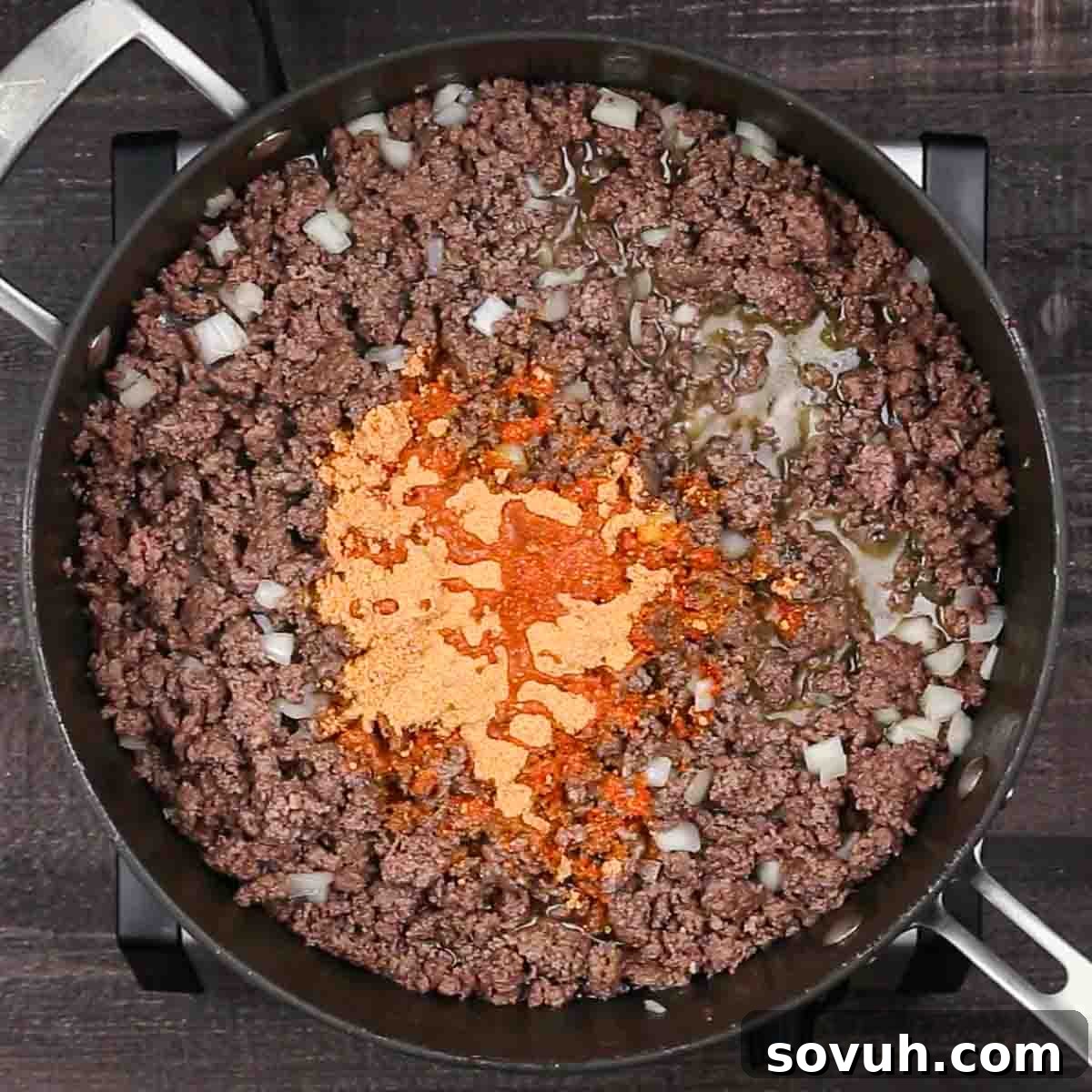 Ground beef and diced onions cooking in a pan with taco seasoning for the enchilada casserole filling.