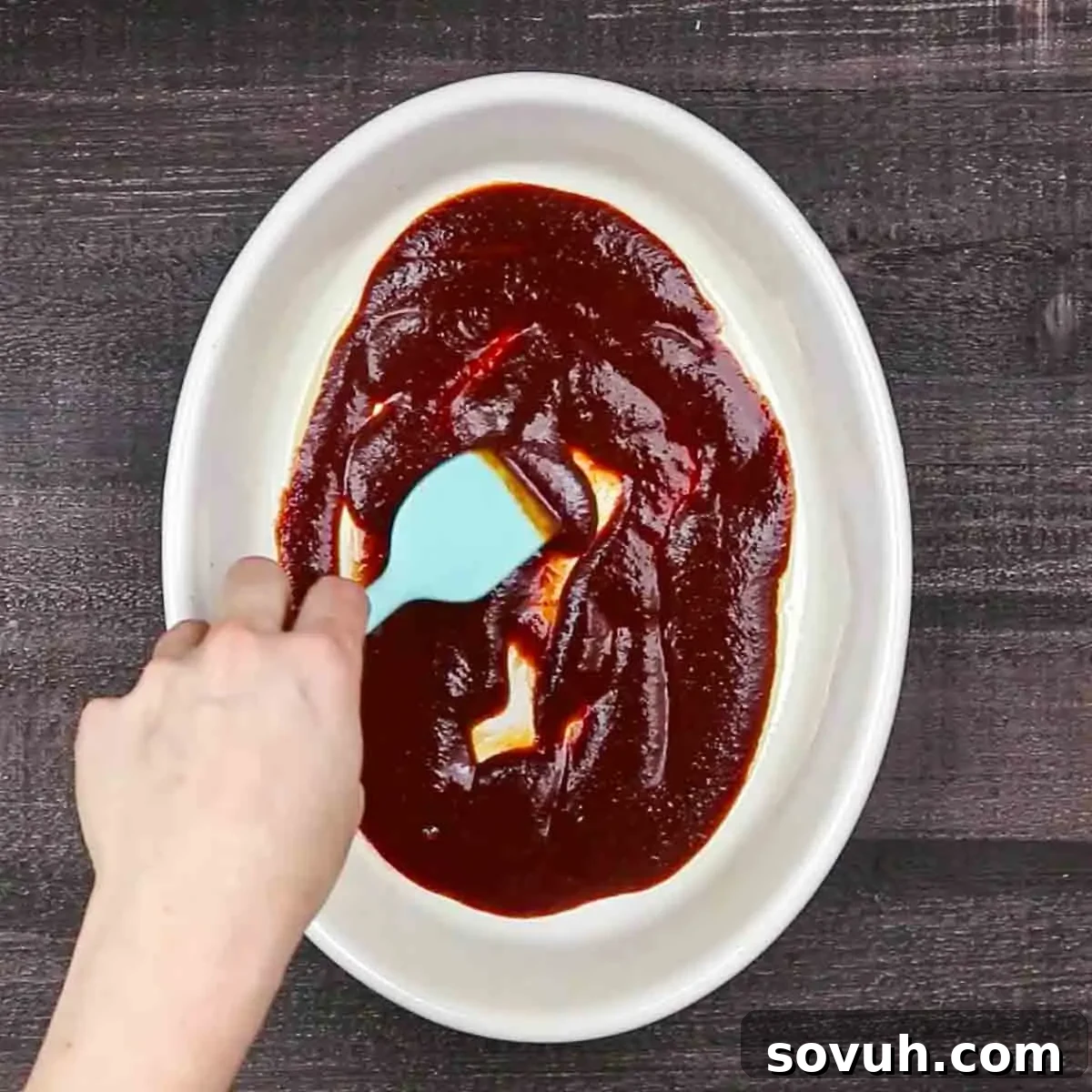 A person pouring rich red enchilada sauce into a bowl, preparing it for layering the casserole.