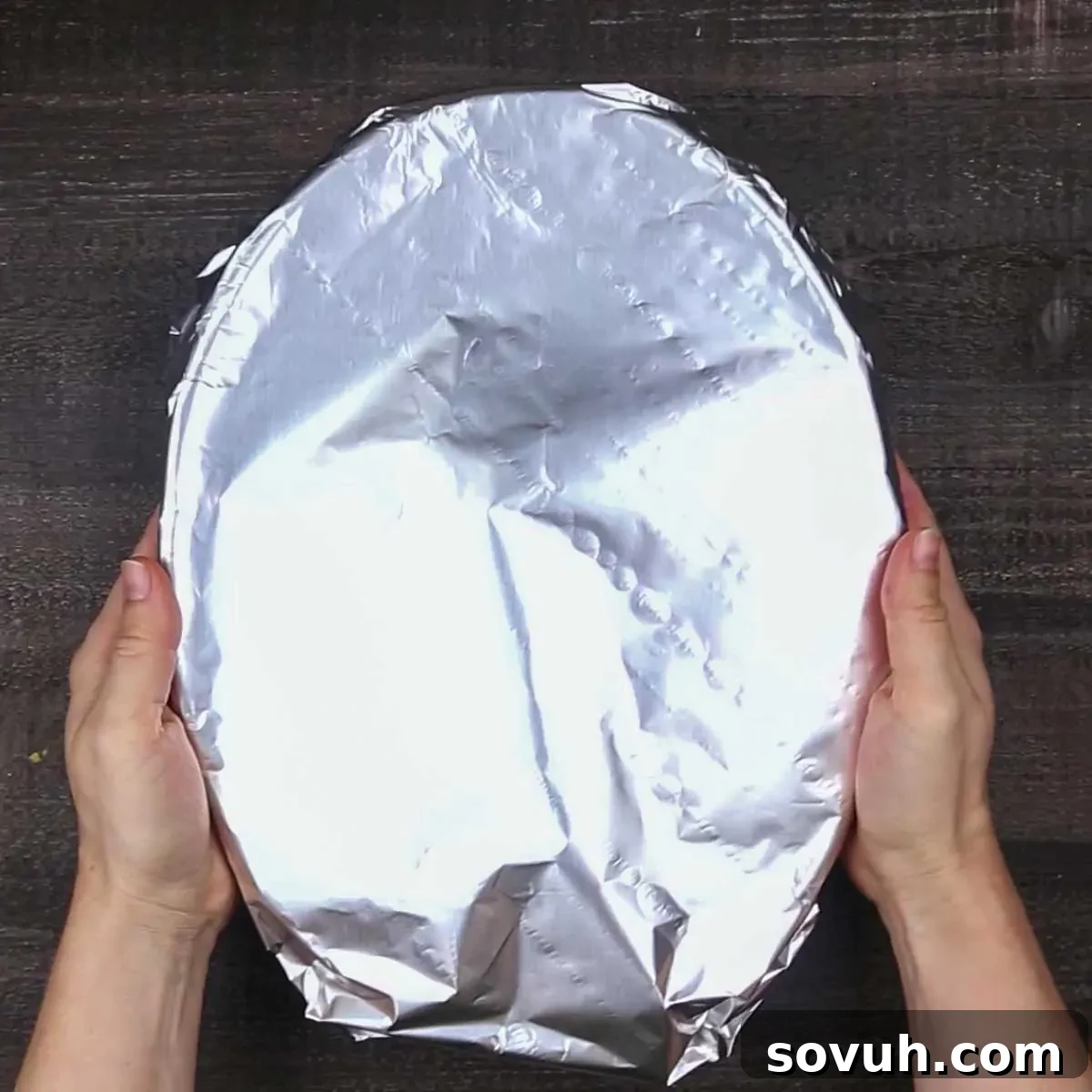 A person covering a baking dish of Beef Enchilada Casserole with aluminum foil, preparing it for baking.