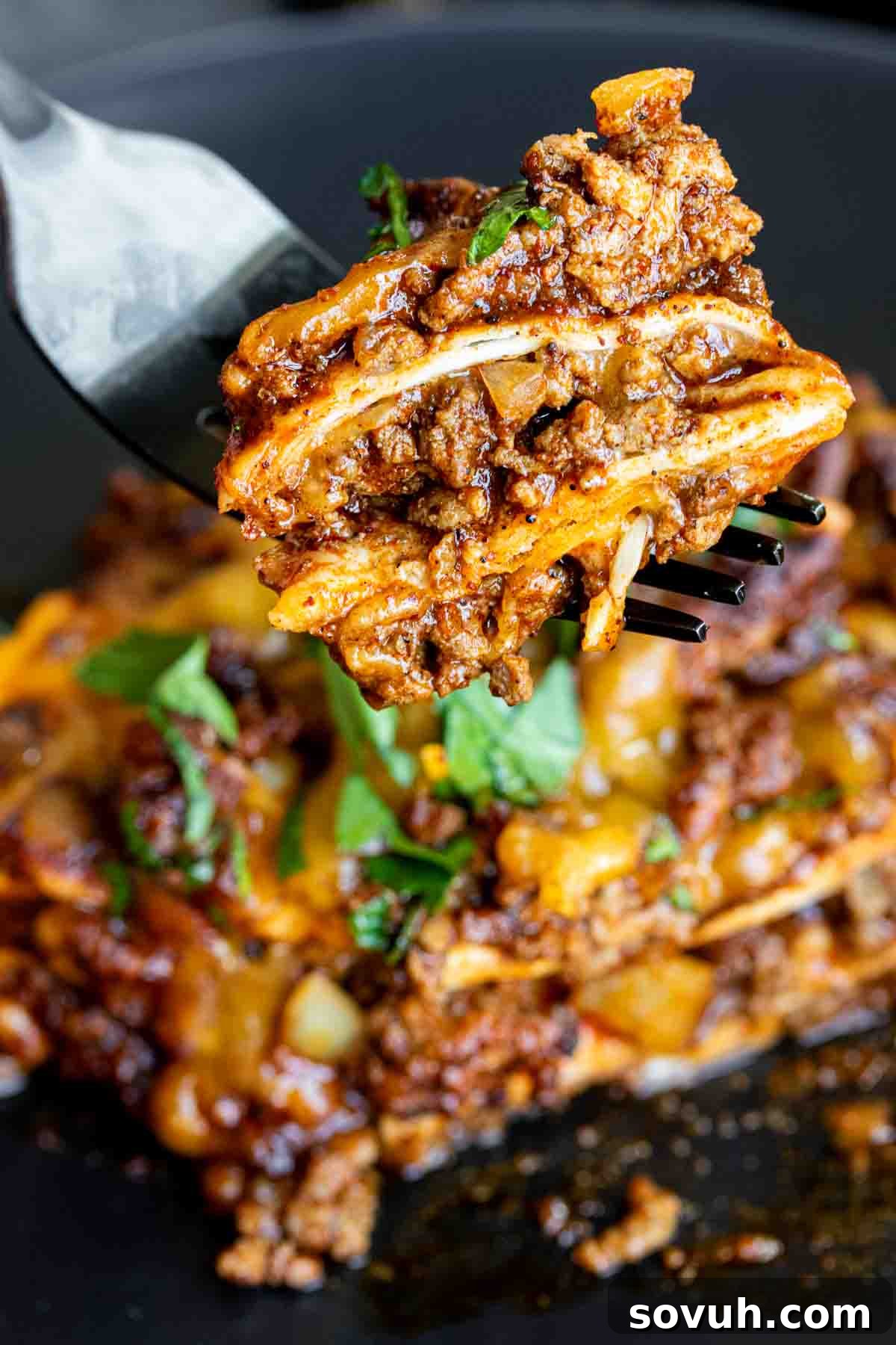 A fork is gently lifting a piece of the rich, cheesy Beef Enchilada Casserole, showing its perfectly baked layers.