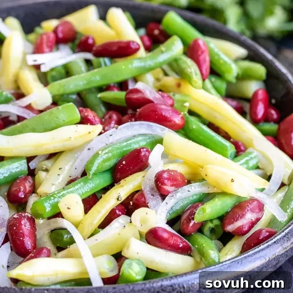 Vibrant Three Bean Salad in a large serving bowl, ready for a summer party. It features green beans, wax beans, and kidney beans in a sweet and tangy dressing.