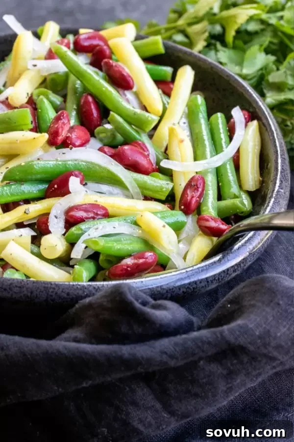 A large ceramic bowl filled with freshly mixed green beans, yellow wax beans, and red kidney beans, showcasing the vibrant colors of the salad.