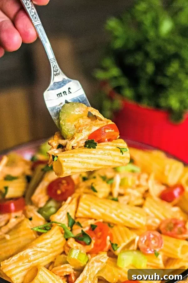 A fork lifts a generous bite of Buffalo Chicken Pasta Salad from a bowl, highlighting the rich texture and vibrant ingredients.