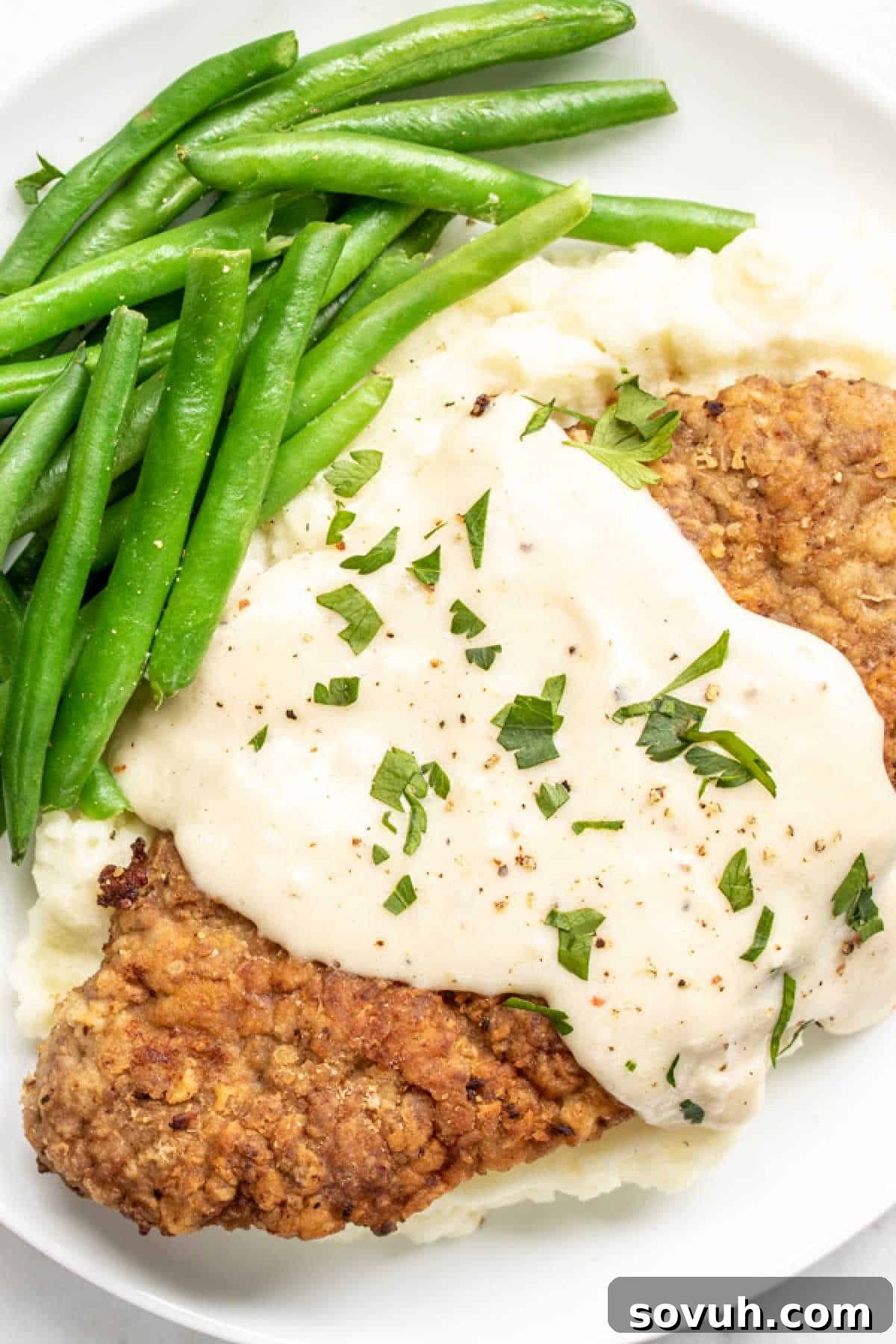 Chicken Fried Steak with Gravy, green beans, and mashed potatoes on a white plate