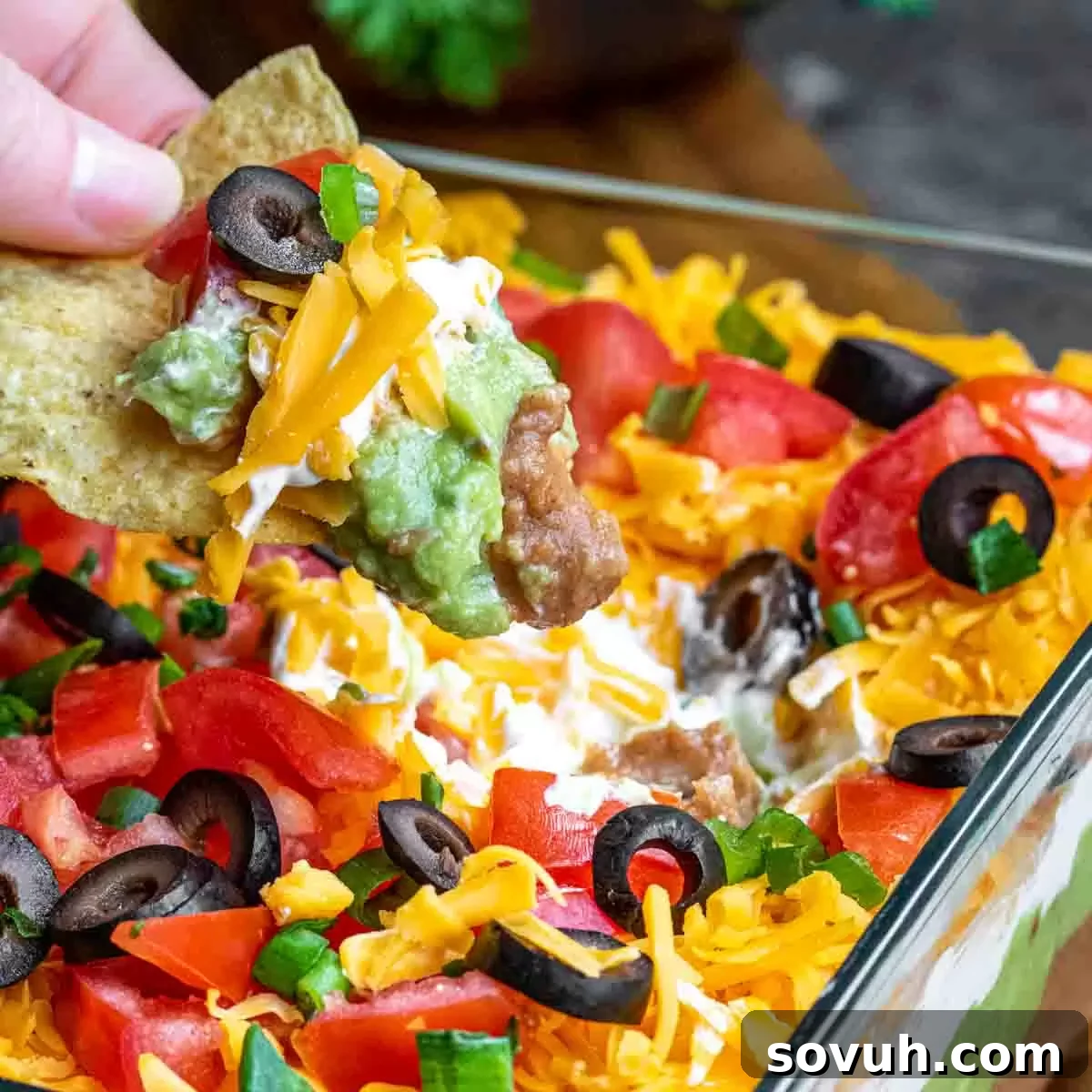 Holding a tortilla chip with Mexican 7 Layer Dip on it, showcasing the vibrant layers