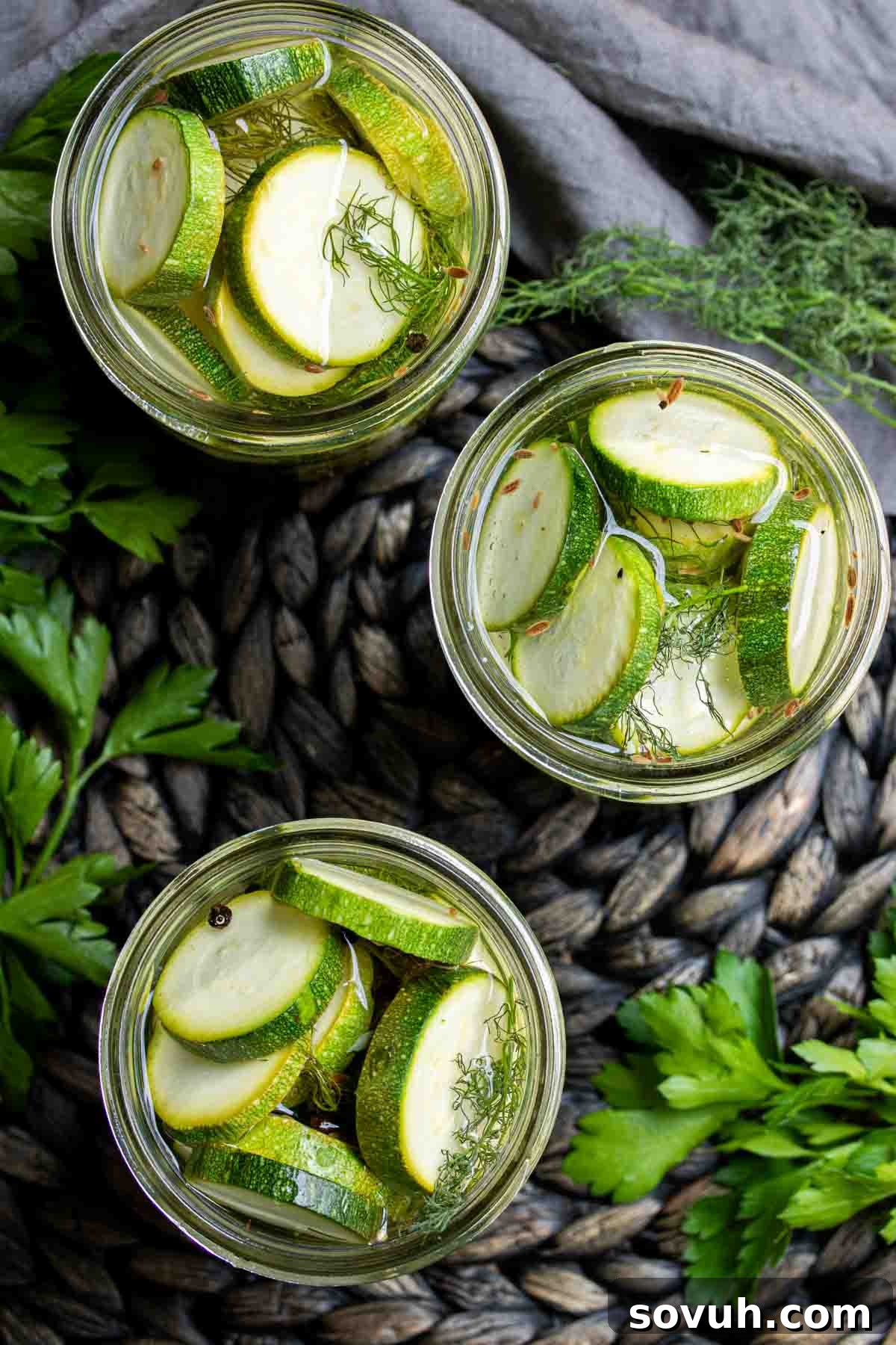 Three mason jars filled with vibrant Quick Pickled Zucchini slices on a rustic wooden surface.