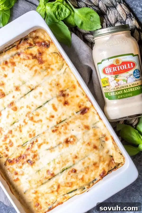 Close-up of a perfectly baked Chicken Alfredo Zucchini Lasagna in a white casserole dish, showing the golden cheese crust and creamy layers.