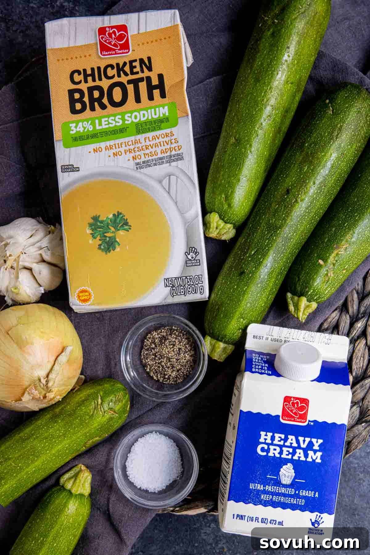 Fresh ingredients laid out on a kitchen counter, including whole zucchini, onions, garlic, and heavy cream, ready for making zucchini soup.