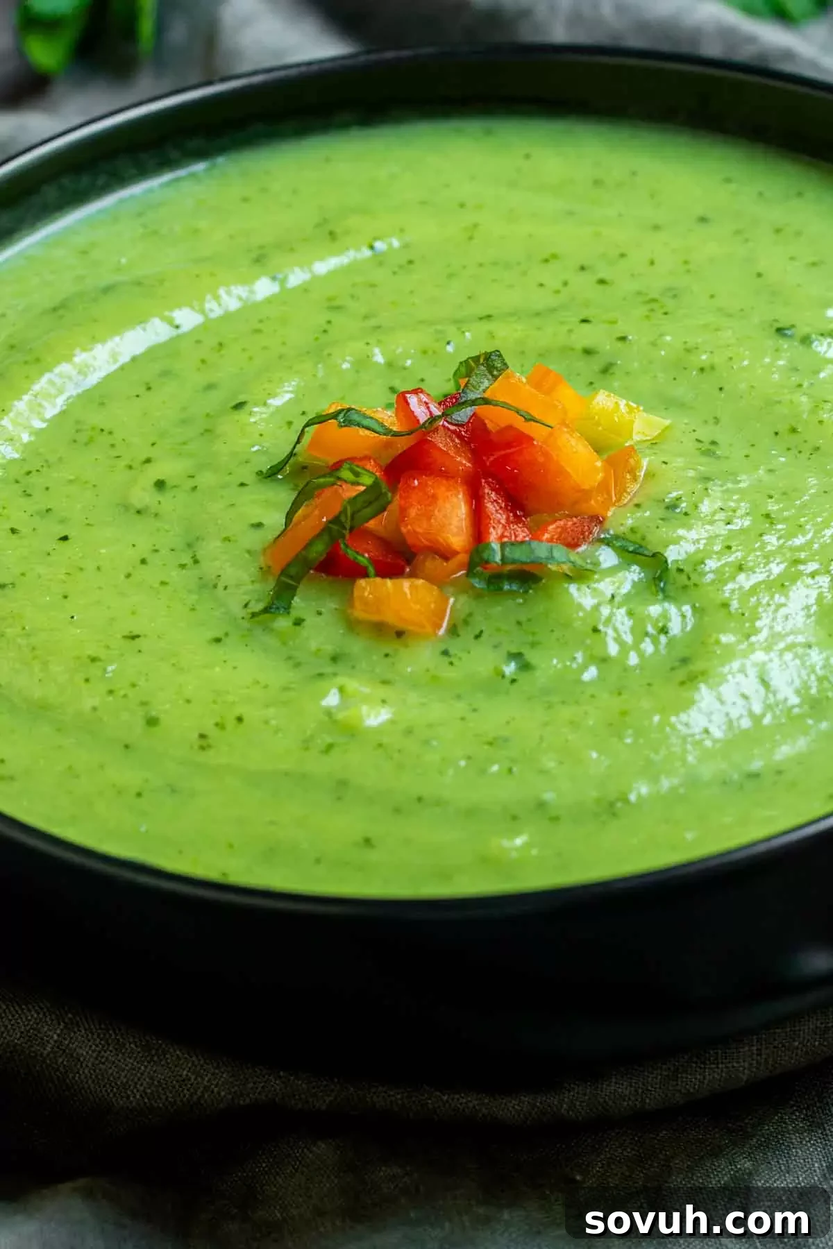 A bowl of creamy zucchini soup, artfully garnished with vibrant, finely chopped bell peppers for a burst of color and flavor.