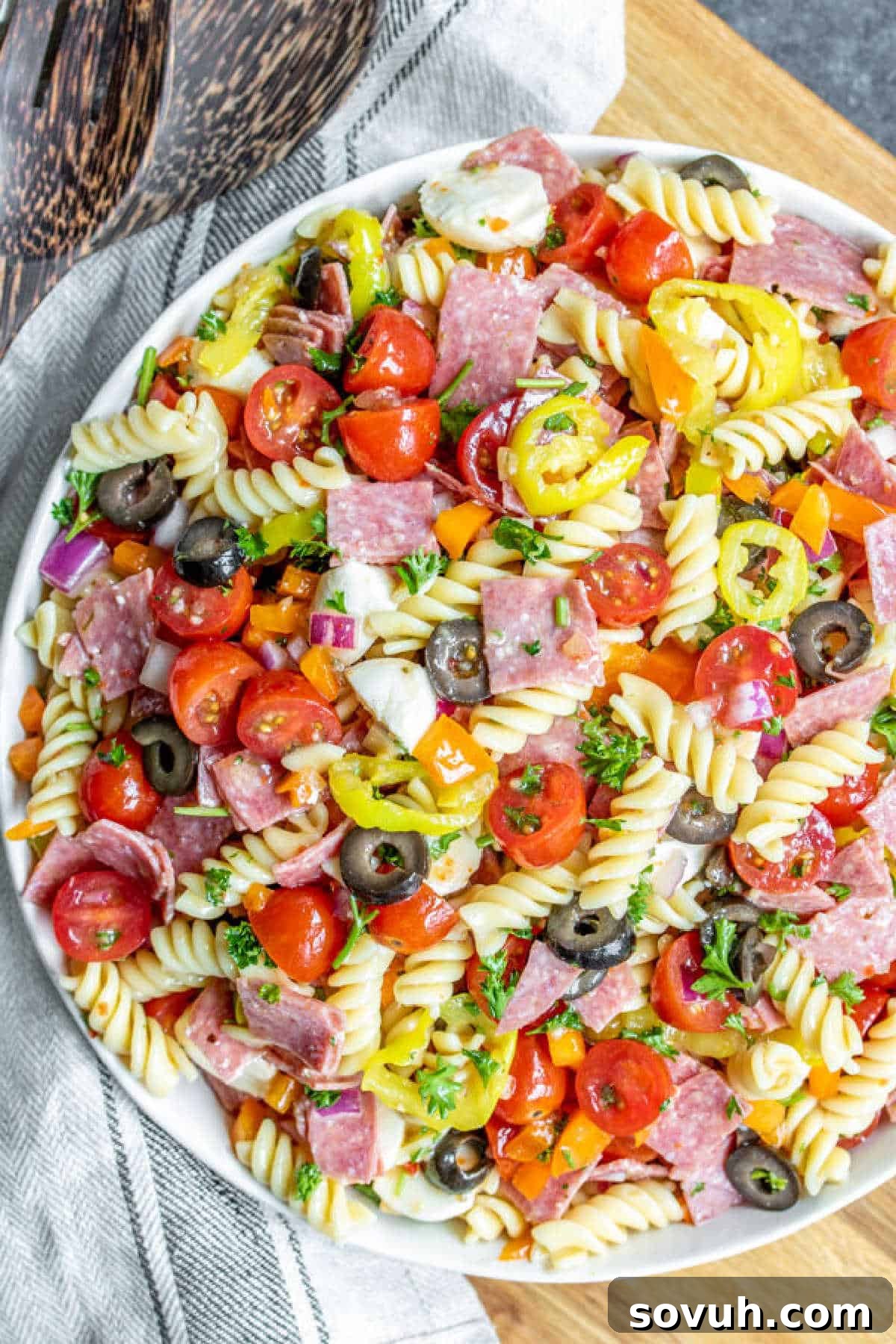 Italian Pasta Salad in a large serving bowl with a wooden spoon and a decorative linen cloth
