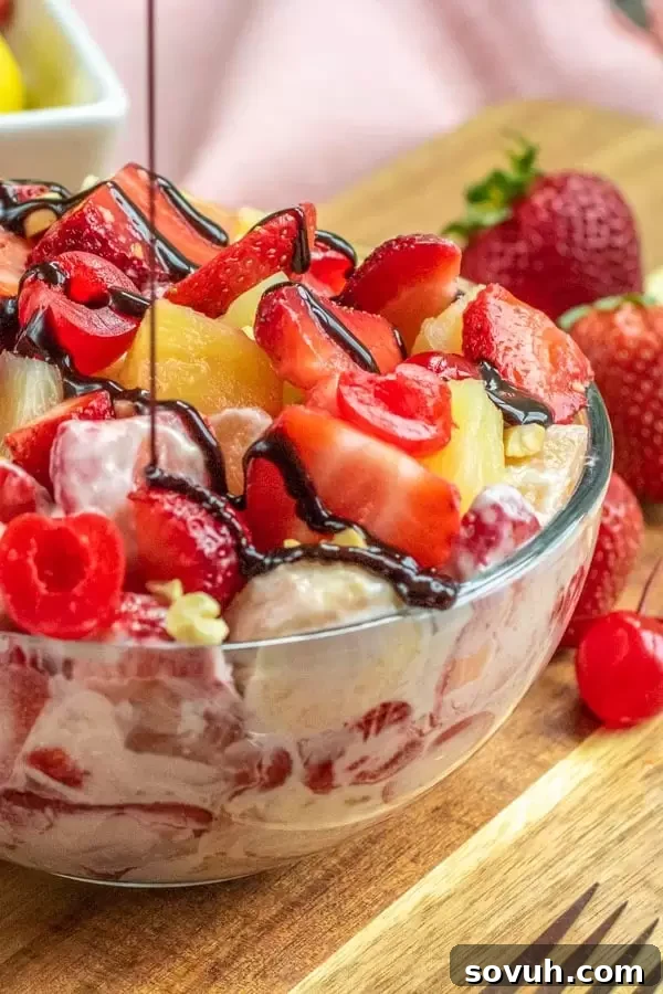 Thick chocolate fudge being artfully drizzled over a vibrant serving of Banana Split Cheesecake Salad, enhancing its dessert appeal.