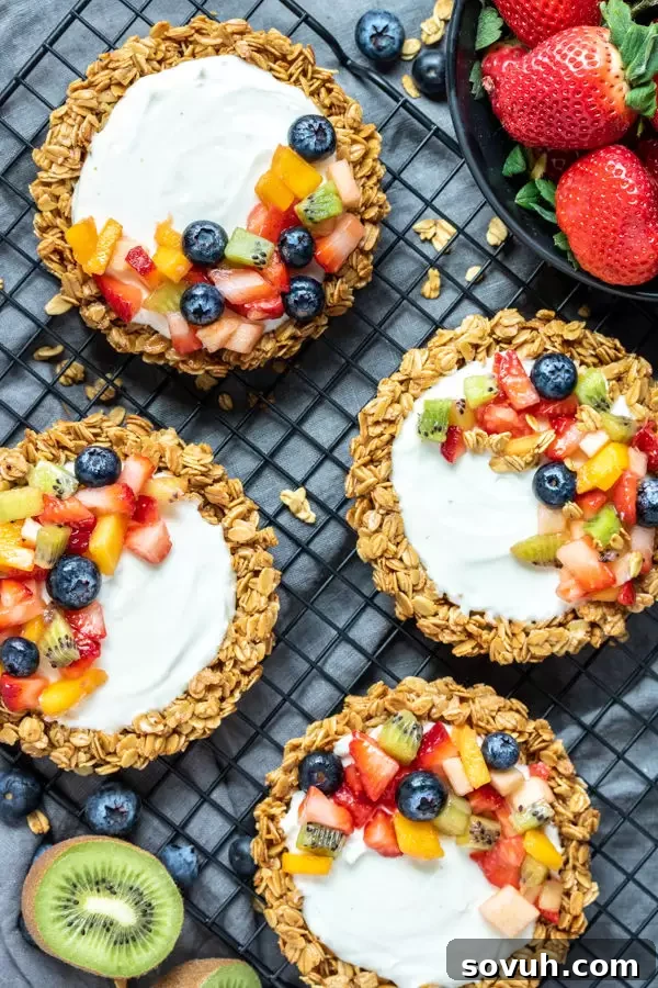 Three mini Granola Fruit Tarts beautifully arranged on a white serving plate, garnished with mint leaves