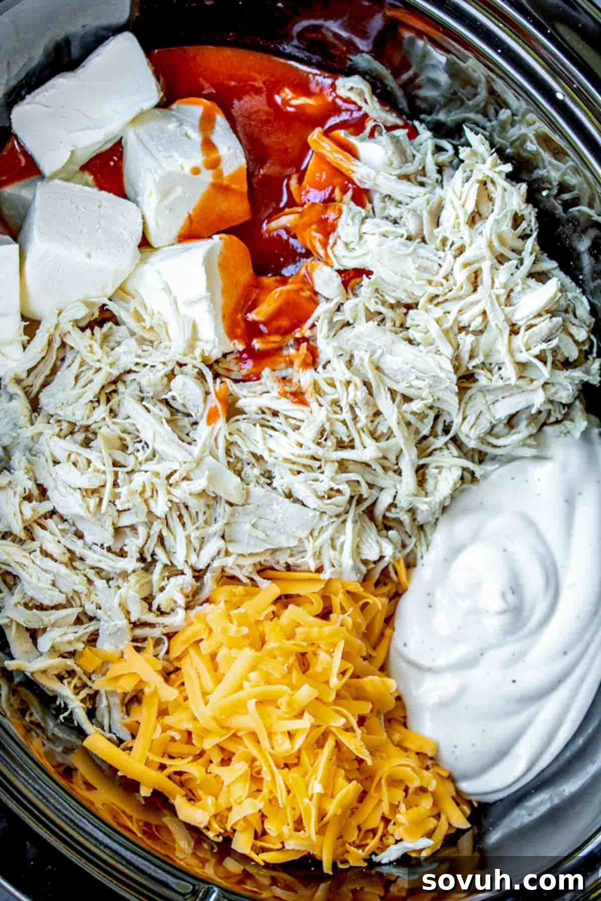 Bowls of shredded chicken, cubed cream cheese, shredded cheddar cheese, buffalo hot sauce, and ranch dressing, ready for mixing.