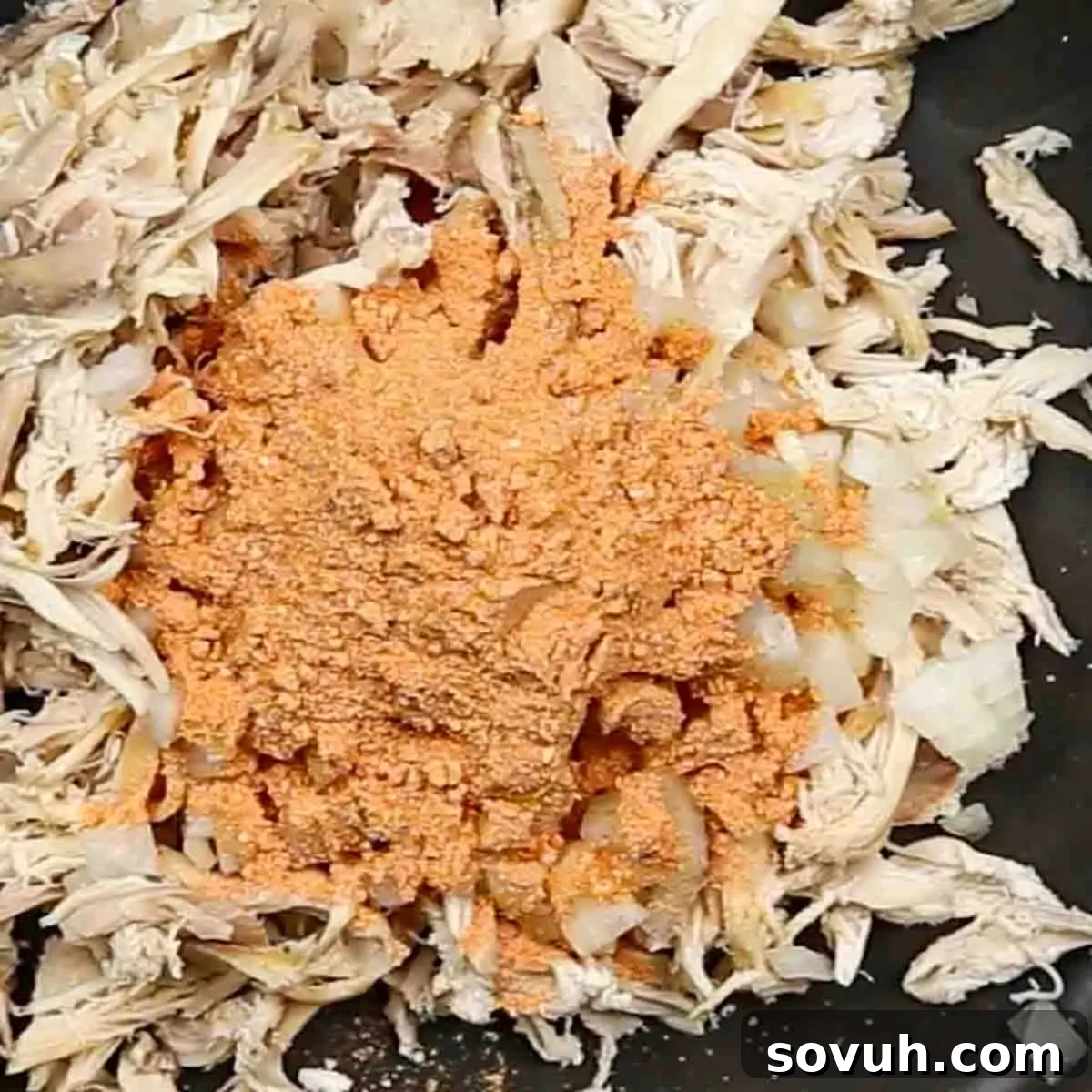 Shredded chicken with diced onions and a pile of orange seasoning powder in a pan.