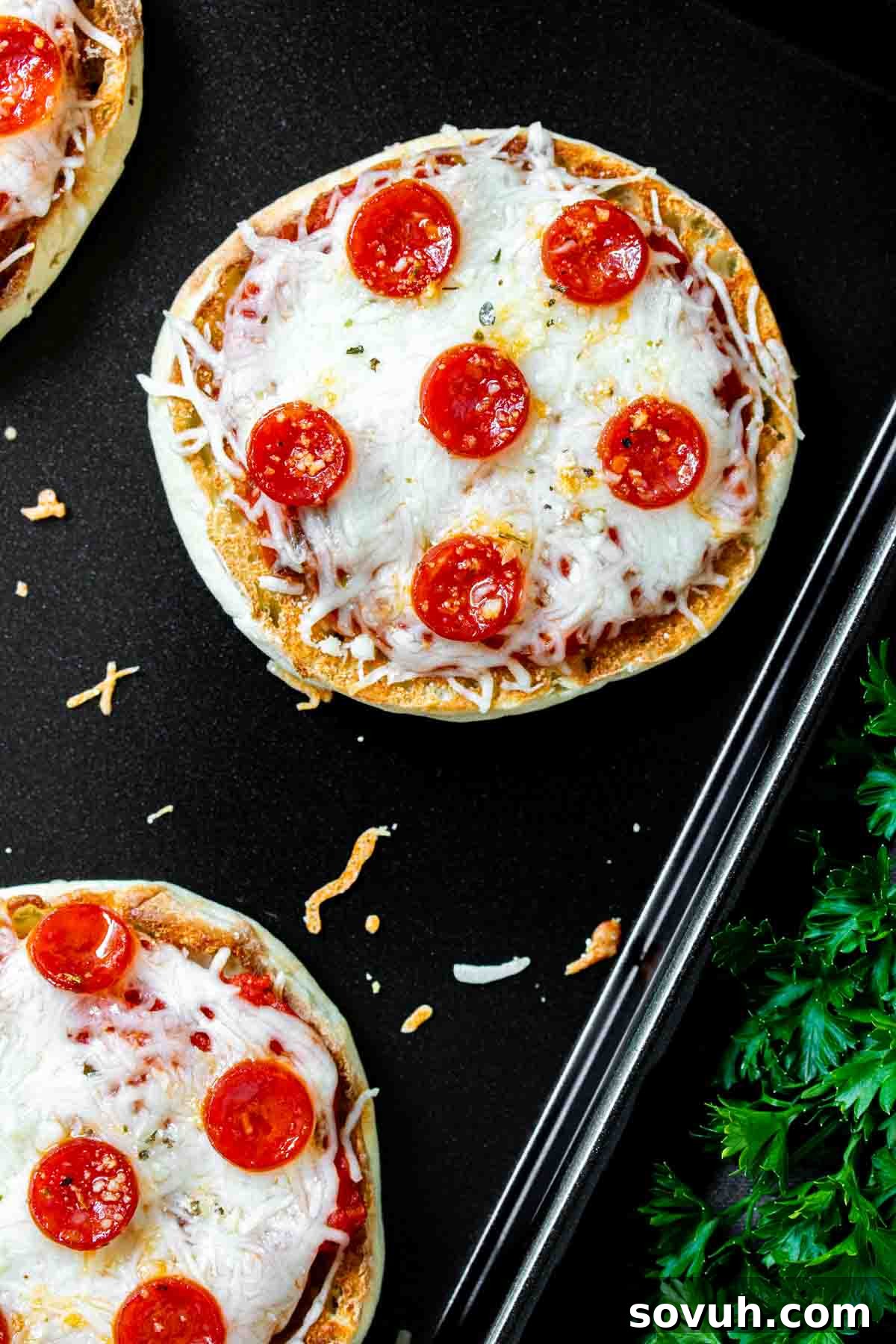 A baking sheet with several English muffin pizzas, some with pepperoni, some plain cheese.