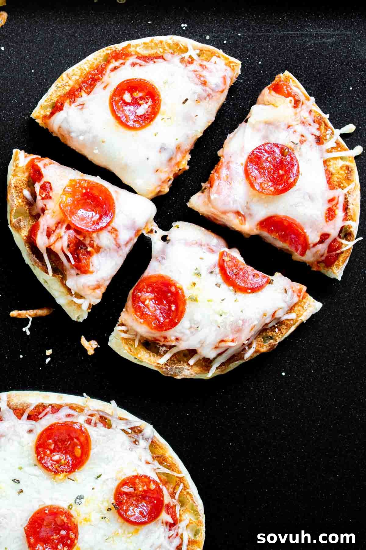 A single English muffin pizza with pepperoni, cheese, and sauce, glistening on a baking sheet.