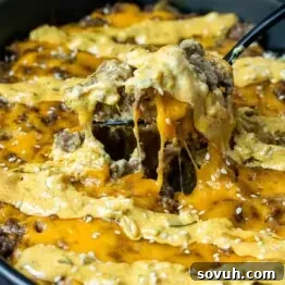 Big Mac Keto Bake 6 A spoon is being lifted out of a Keto Big Mac Casserole dish, highlighting its rich texture and topping.