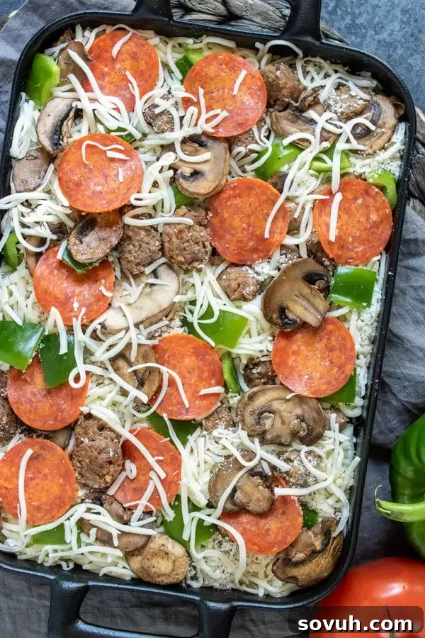 Uncooked Low Carb Pizza Casserole showing layers of cauliflower, meat, vegetables, and cheese before baking