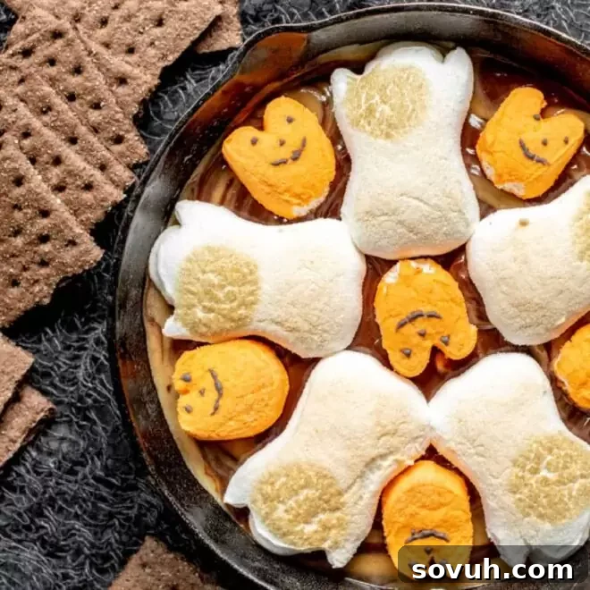 A cast iron skillet filled with bubbling Halloween S'mores Dip, ready for dipping.