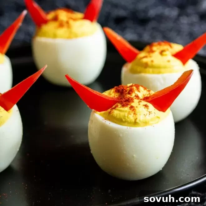 Halloween Deviled Eggs, creatively decorated with red horns, served on a black plate.