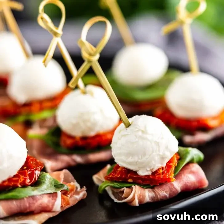 Caprese skewers with mozzarella, basil, and tomato on prosciutto slices, presented on a black plate.