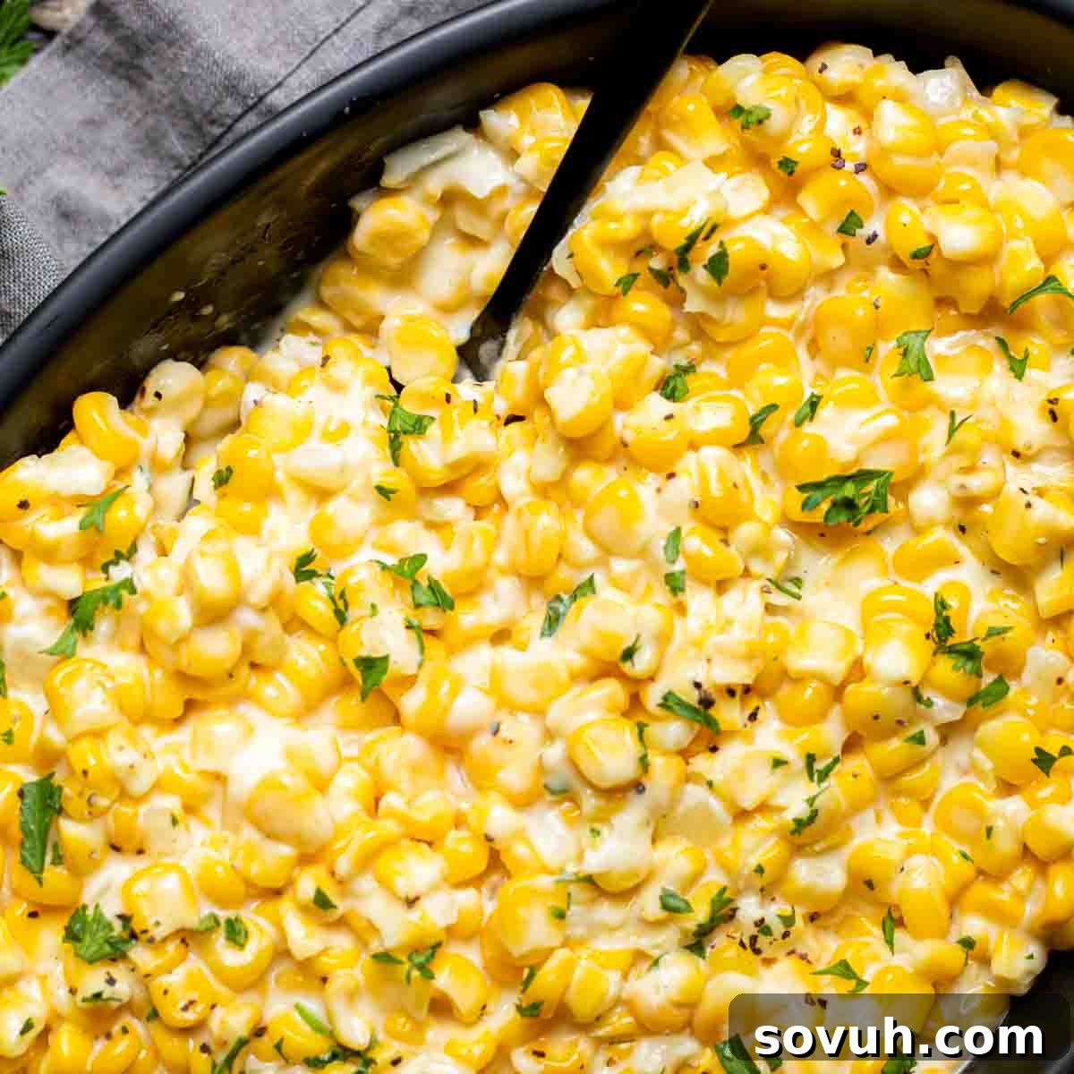 Creamed Corn in a black dish with a spoon, highlighting its creamy texture.