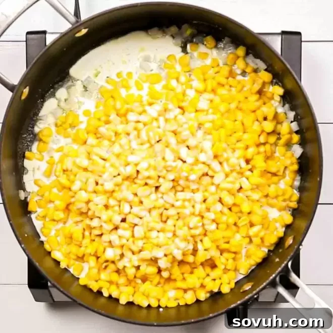 A frying pan filled with all the ingredients for Creamed Corn simmering on the stovetop.