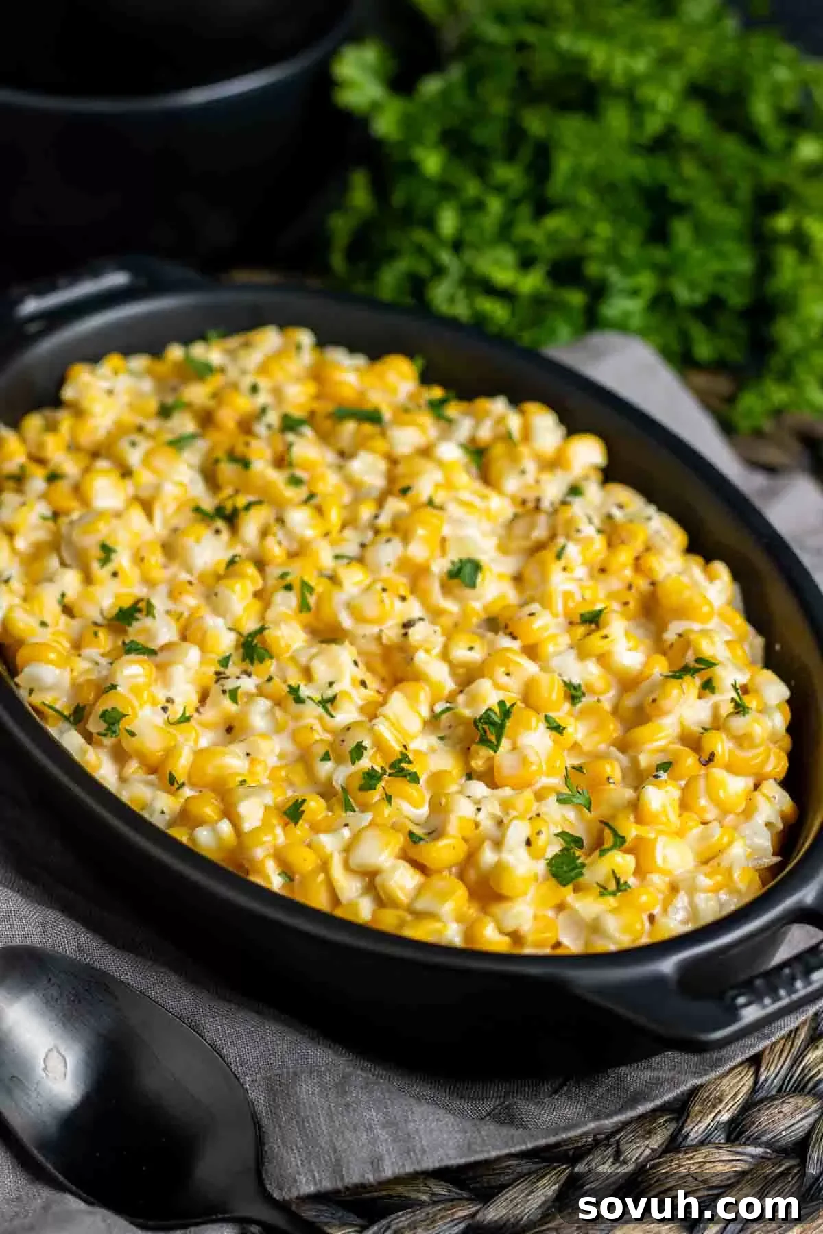 A black dish full of homemade Creamed Corn, garnished slightly.