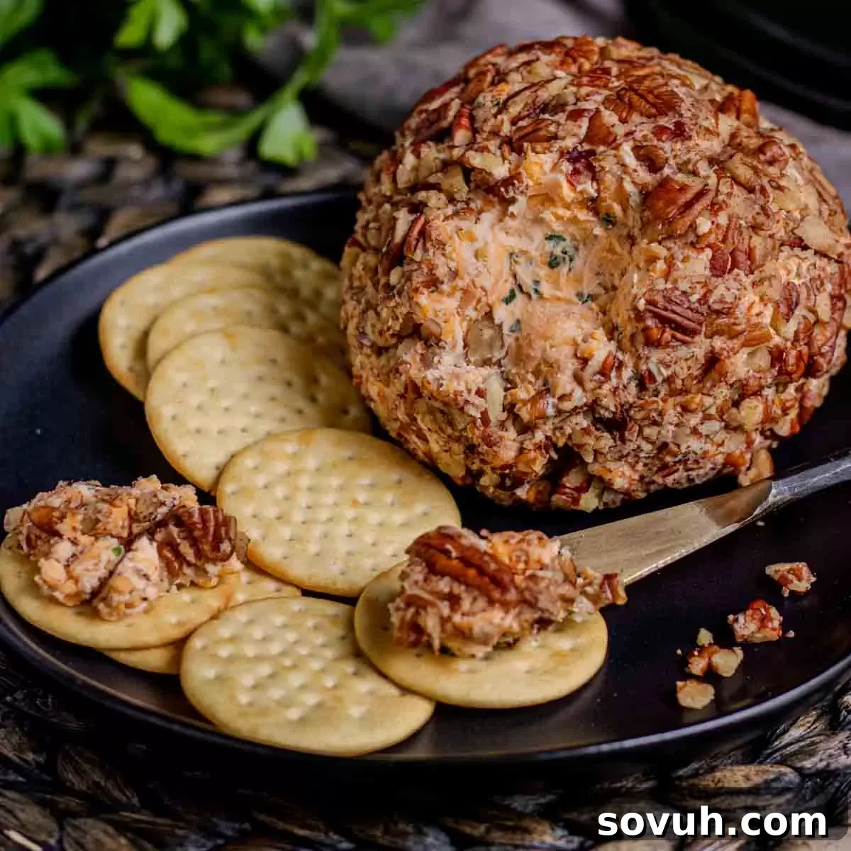 A cheese ball with crackers and pecans on a black plate, perfect for holidays.