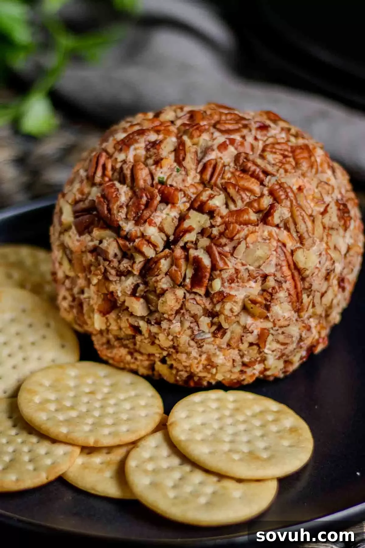 Pecan cheese ball on a black plate with crackers for a party.