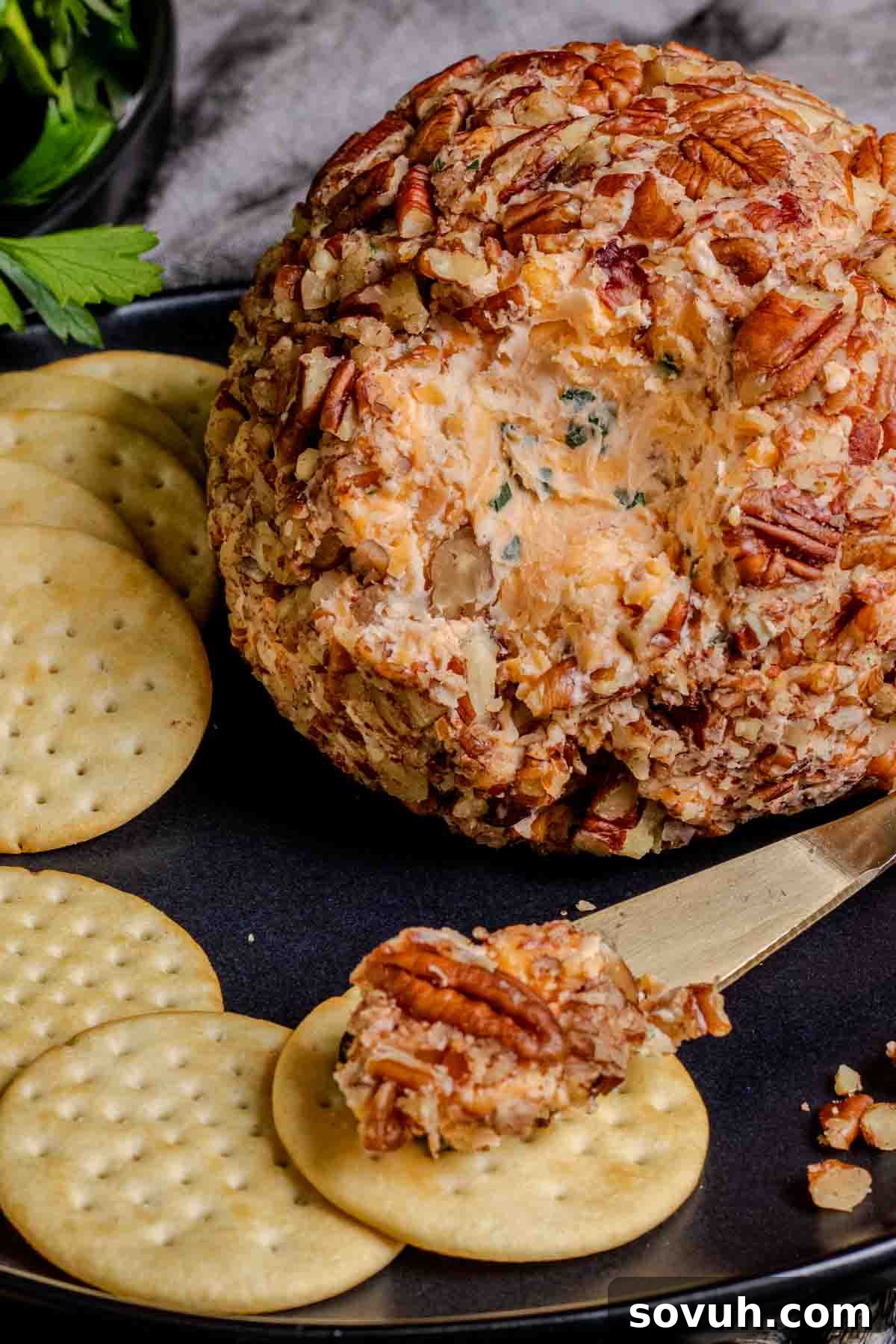A cheese ball with crackers and nuts on a plate, ready to serve.