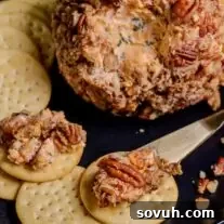 A cheese ball with pecans and crackers on a plate.