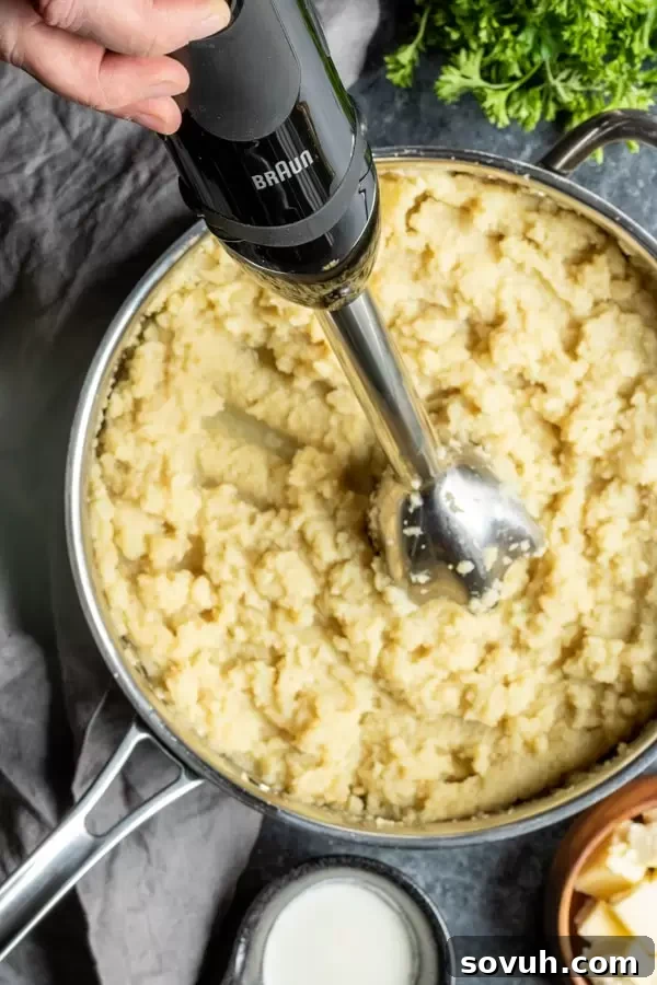 Cauliflower mash being made in a skillet, showcasing the pureeing process with a hand blender.