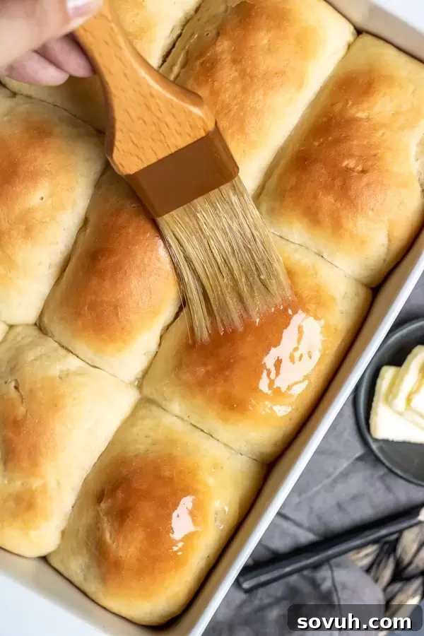 Brushing melted butter onto warm, homemade Overnight Refrigerator Yeast Rolls for a glossy finish.