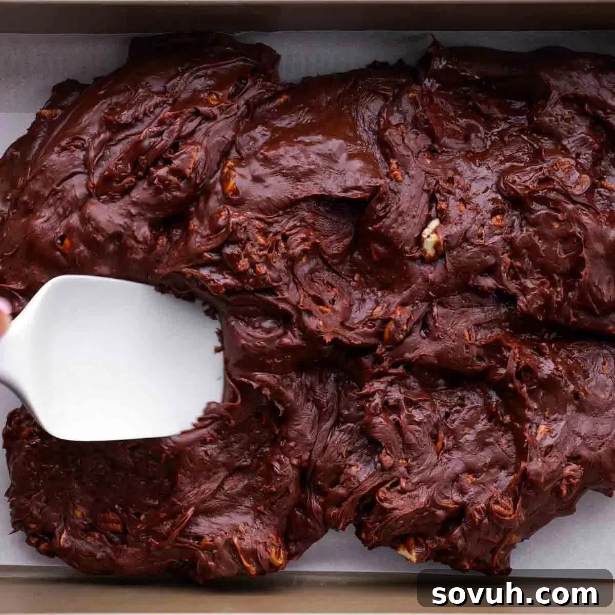 spreading Easy Microwave Fudge with chopped pecans and white spatula