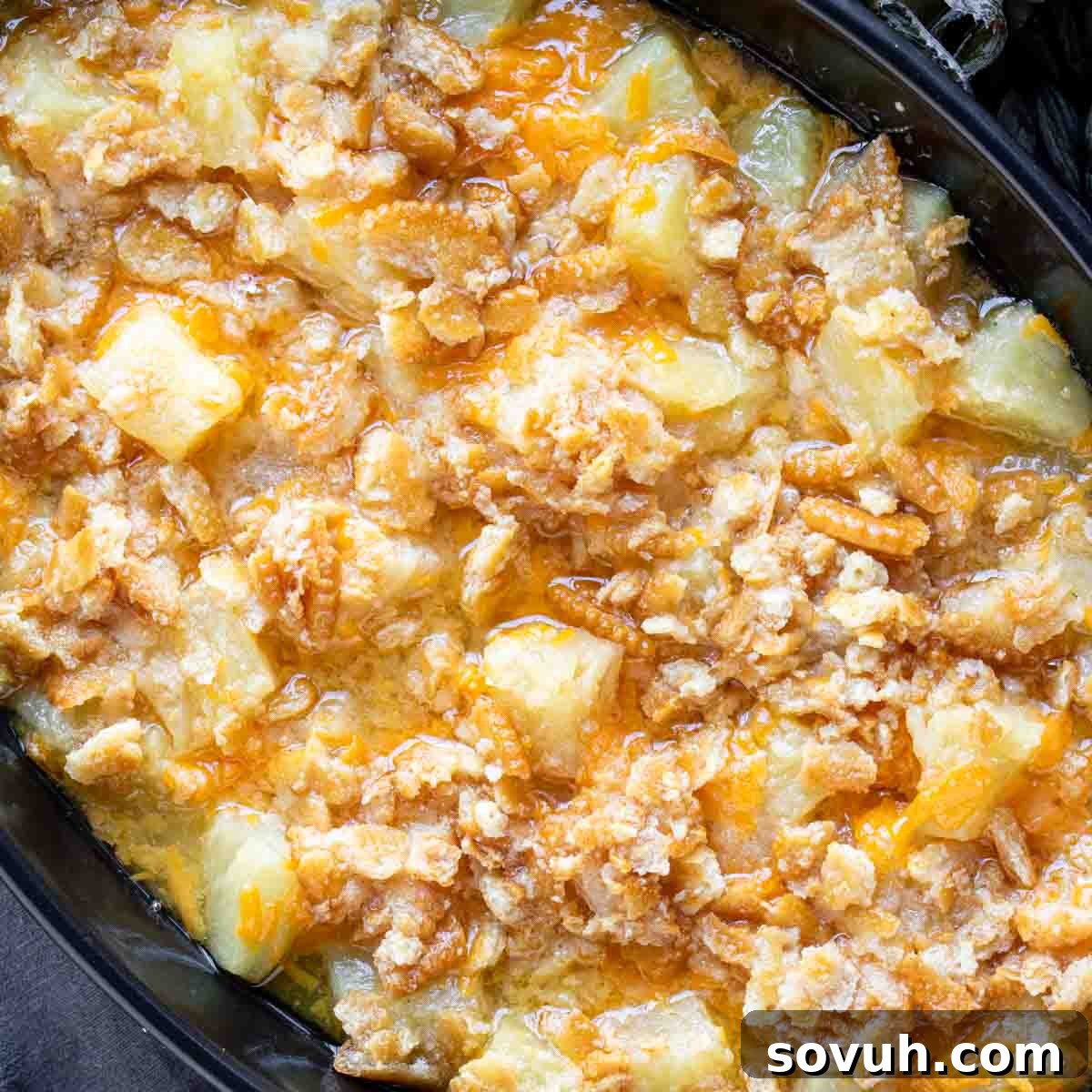A golden-brown pineapple casserole in a black baking dish, ready to be served, perfect for a holiday feast.