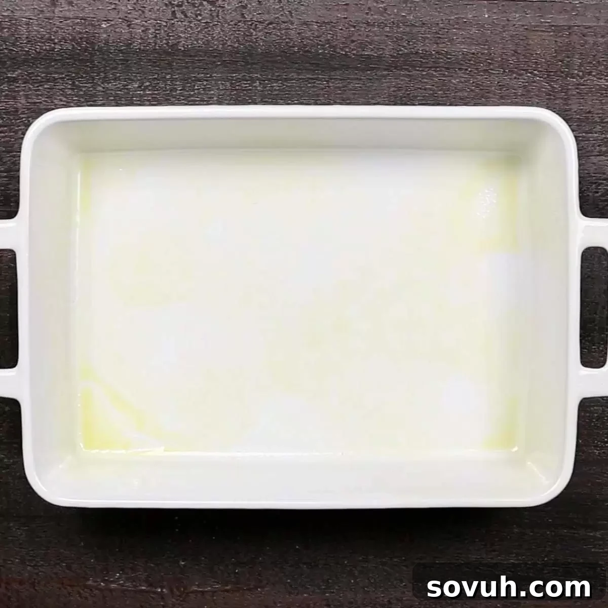 An empty white rectangular baking dish, lightly greased and ready for the casserole mixture.