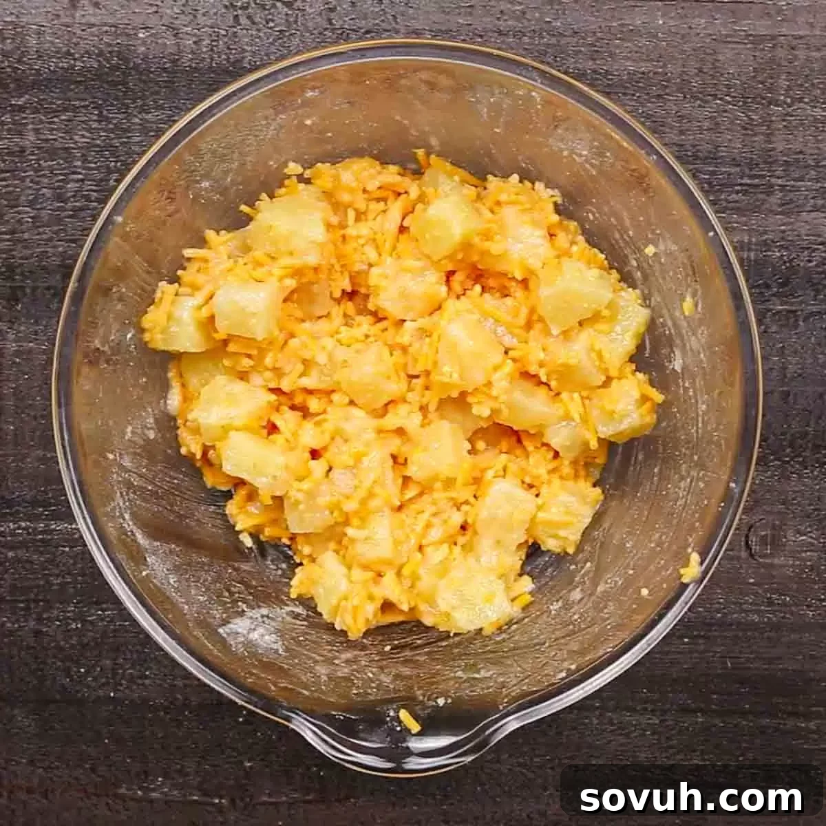 A glass mixing bowl filled with shredded cheddar cheese and pineapple chunks, illustrating the main casserole mixture.