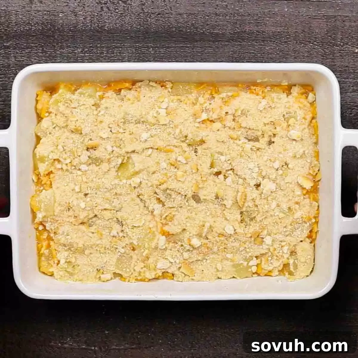 A white casserole dish filled with the pineapple and cheese mixture, topped with the buttery Ritz cracker crumbs, ready for baking.