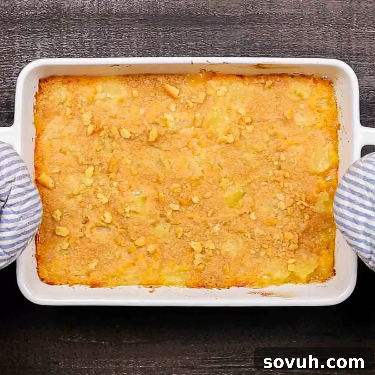 A freshly baked golden pineapple casserole in a dish, with a hand reaching towards it, symbolizing readiness to serve.