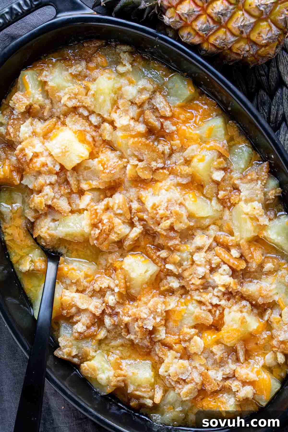 A black skillet filled with pineapple casserole and a serving spoon, highlighting the warm, bubbly texture.