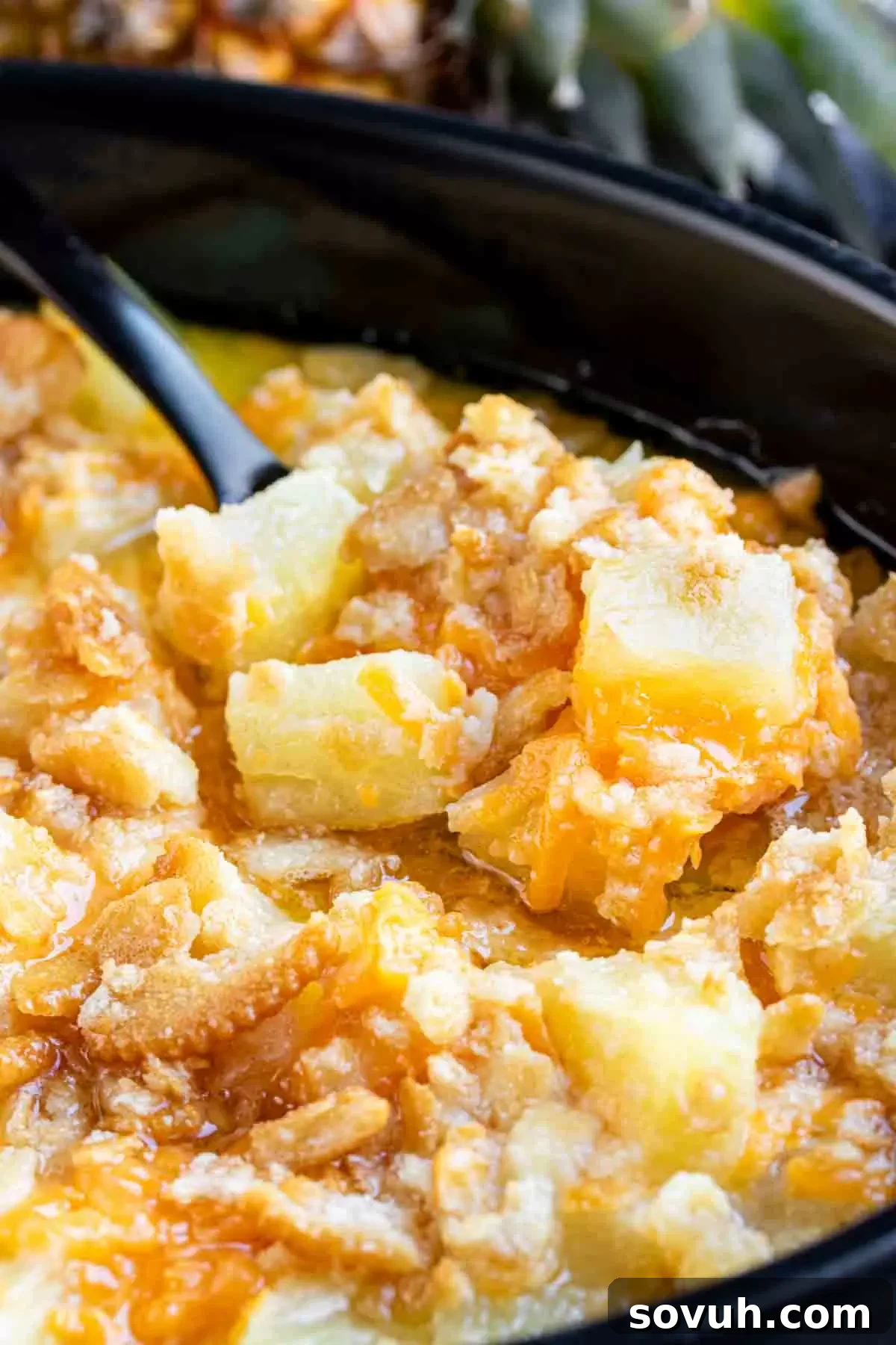 A bowl filled with golden cheesy pineapple casserole and a spoon, ready to be eaten, showcasing its inviting texture.