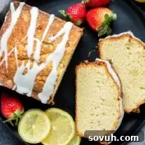 Lemon pound cake with strawberries and icing on a black plate.