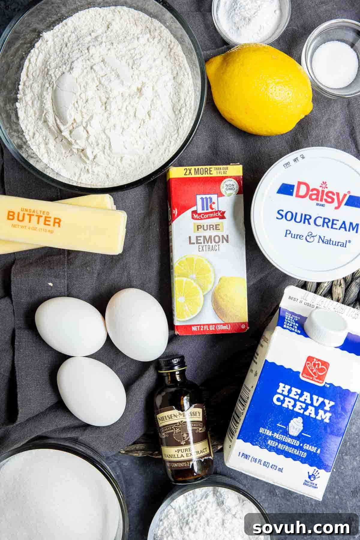 Various ingredients for a lemon cake laid out neatly on a table, including lemons, butter, eggs, flour, and sugar.